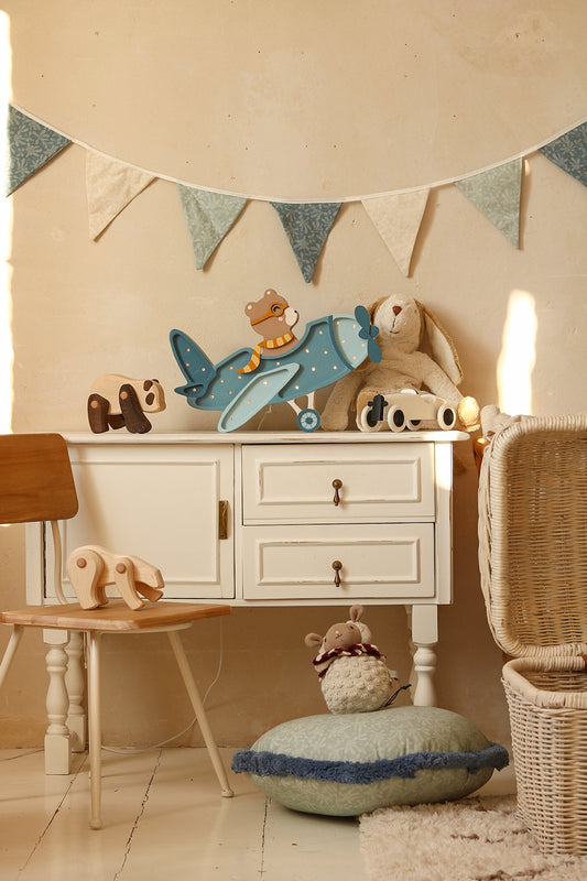 Veilleuse avion en bois ourson placée sur une commode dans une chambre de bébé. Modèle bleu.