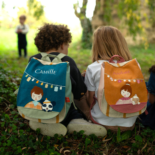 Enfants assis avec sacs à dos maternelle personnalisés, collection Oiseau Bateau. Sac à dos bleu, sac à dos jaune.