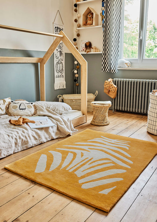 Inspiration déco chambre enfant sur le thème nature et jungle. Tapis zèbre en coton bio, couleur jaune abricot. Mixe parfait avec le bois, le blanc cassé et le vert sauge. Bleuu-Studio.
