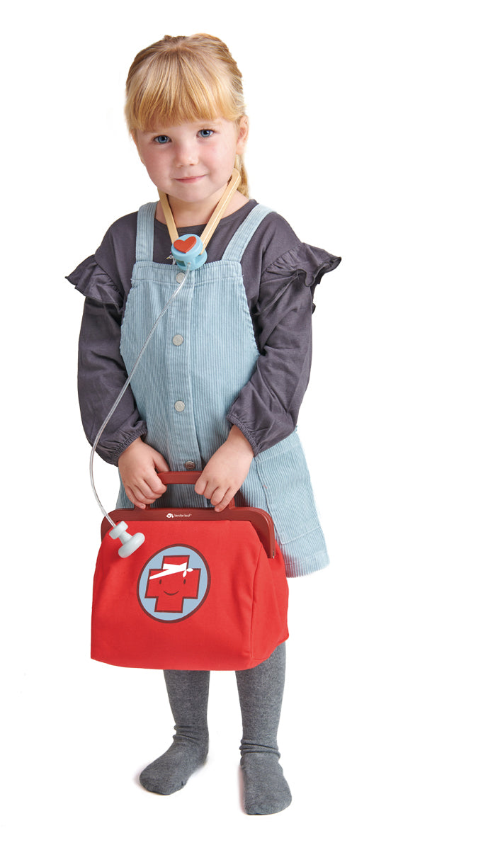 Petite fille portant fièrement sa malette de docteur, stéthoscope autour du cou prête à soigner les bobos des doudous et des poupées et à prendre soin d'eux.