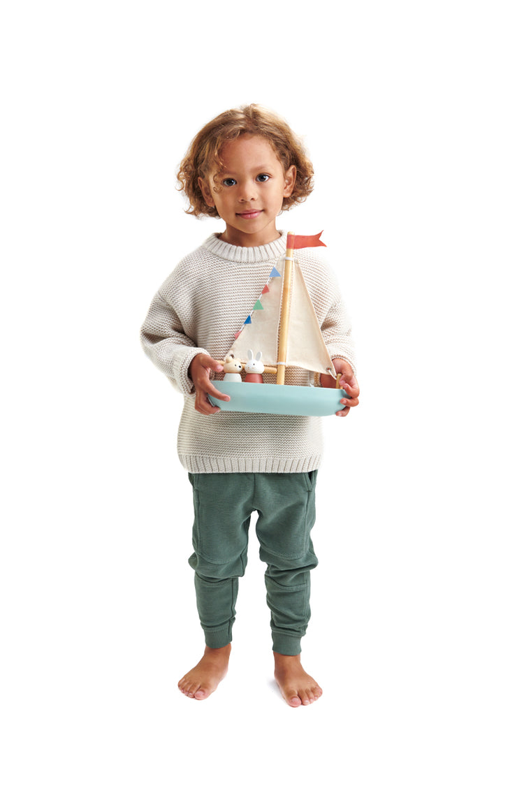 Petit garçon portant fièrement son bateau en bois Tender Leaf, prêt à jouer et à imaginer de merveilleuses aventures avec les deux personnages Squeak et Bubble.