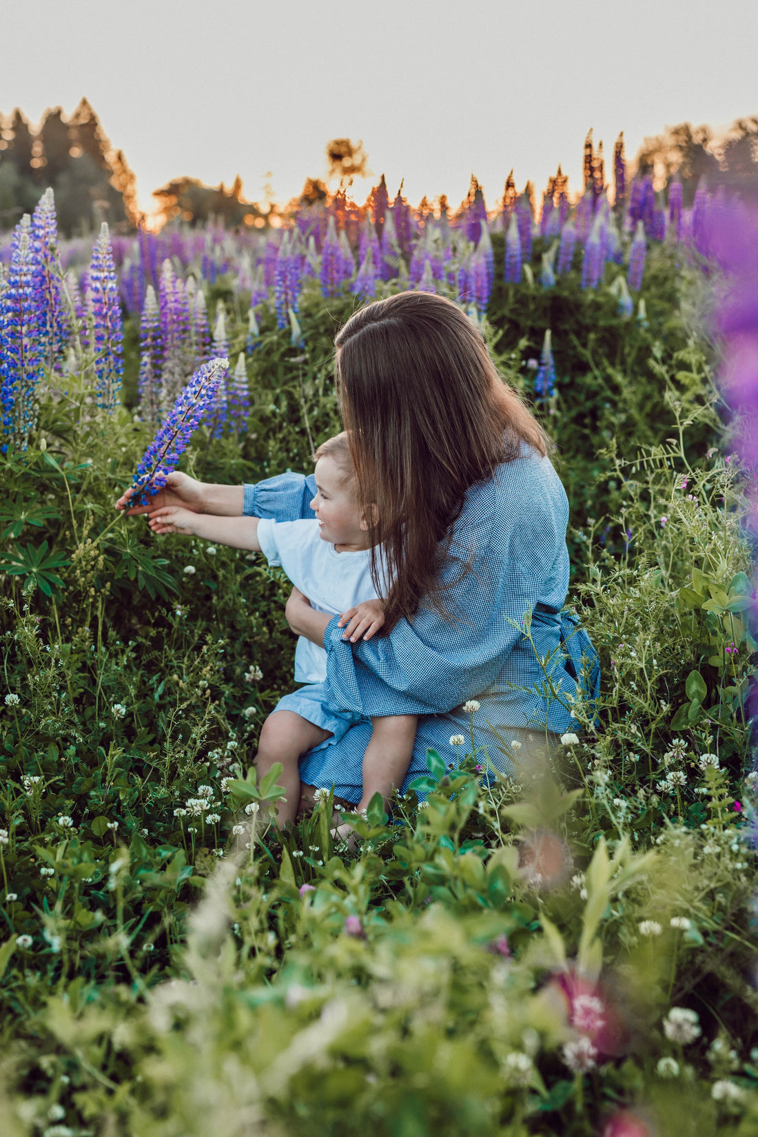 Bébé dans les bras de sa maman au milieu d'un champ de fleurs violettes. Eveil en nature. Photo de Liana Mikah, source Unsplash.