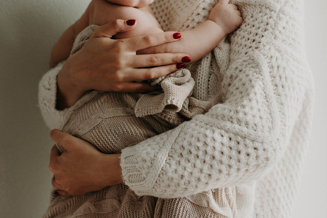 Maman tenant son bébé dans les bras. Féminité marquée avec des ongles vernis rouge. 
