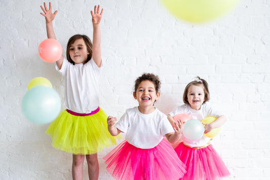 3 petites filles, déguisées en jupe fluo jaune et rose, s'amusent à lancer des ballons à paillettes Ratatam. Eclats de rire et joie de vivre.  