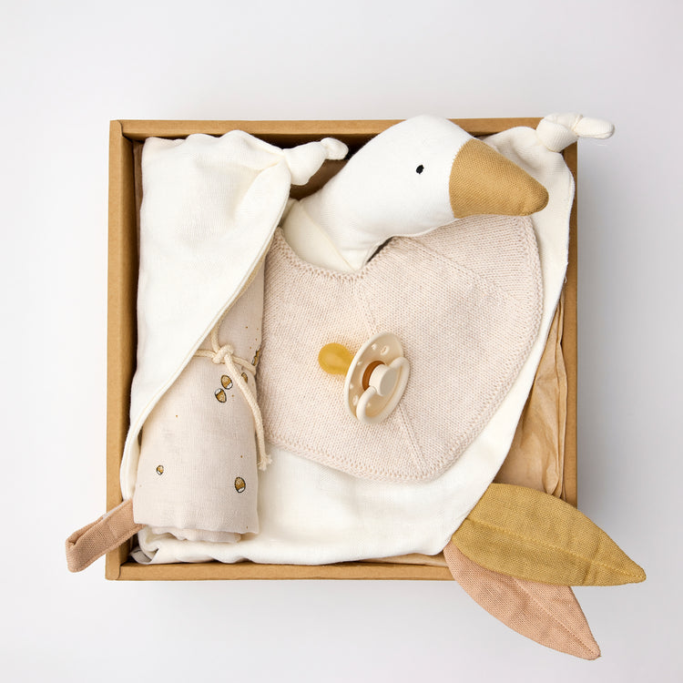 Coffret naissance en coton bio de couleur vanille/écru : dans un packaging carton recyclé, un doudou lange en coton bio, un bavoir tricot, une tétine frigg et un lange en coton bio.