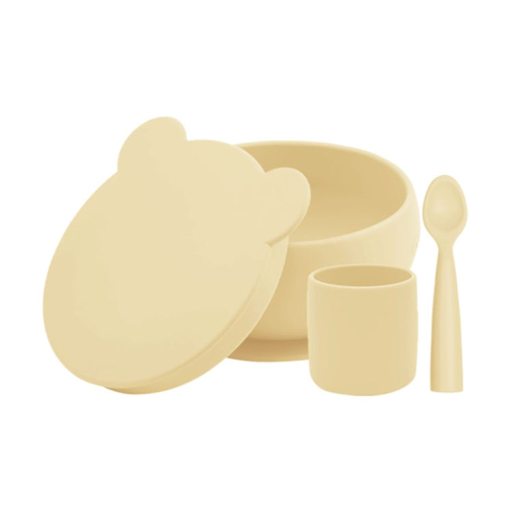 Coffret de vaisselle pour bébé en silicone, avec un bol à ventouse et son couvercle avec de petites oreilles d'ours, un gobelet et une cuillère ergonomique. Couleur jaune pastel, miel.