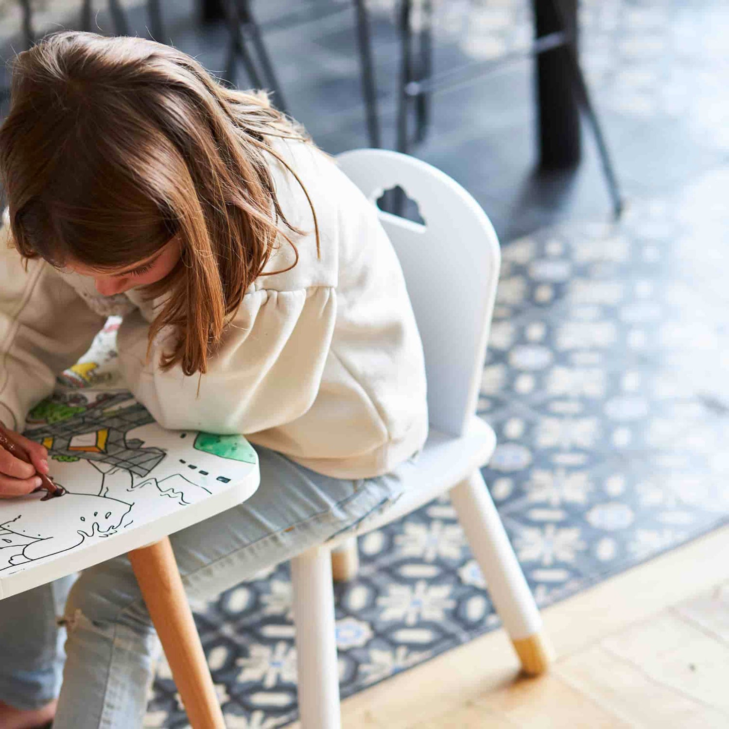 Petite fille concentrée sur son coloriage à la table coloriage enfant
