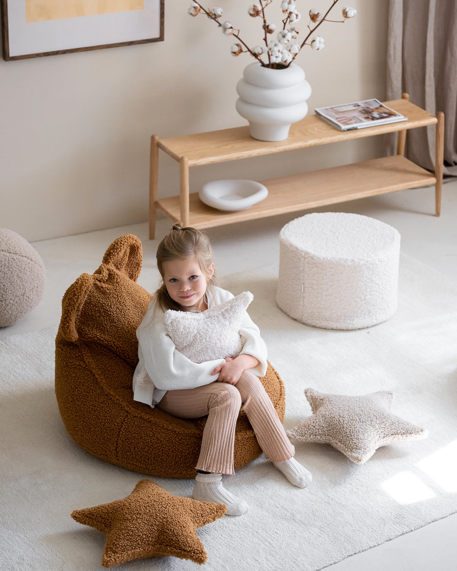 Fille assise avec un coussin étoile en peluche Wigiwama sur un fauteuil en forme d'ourson