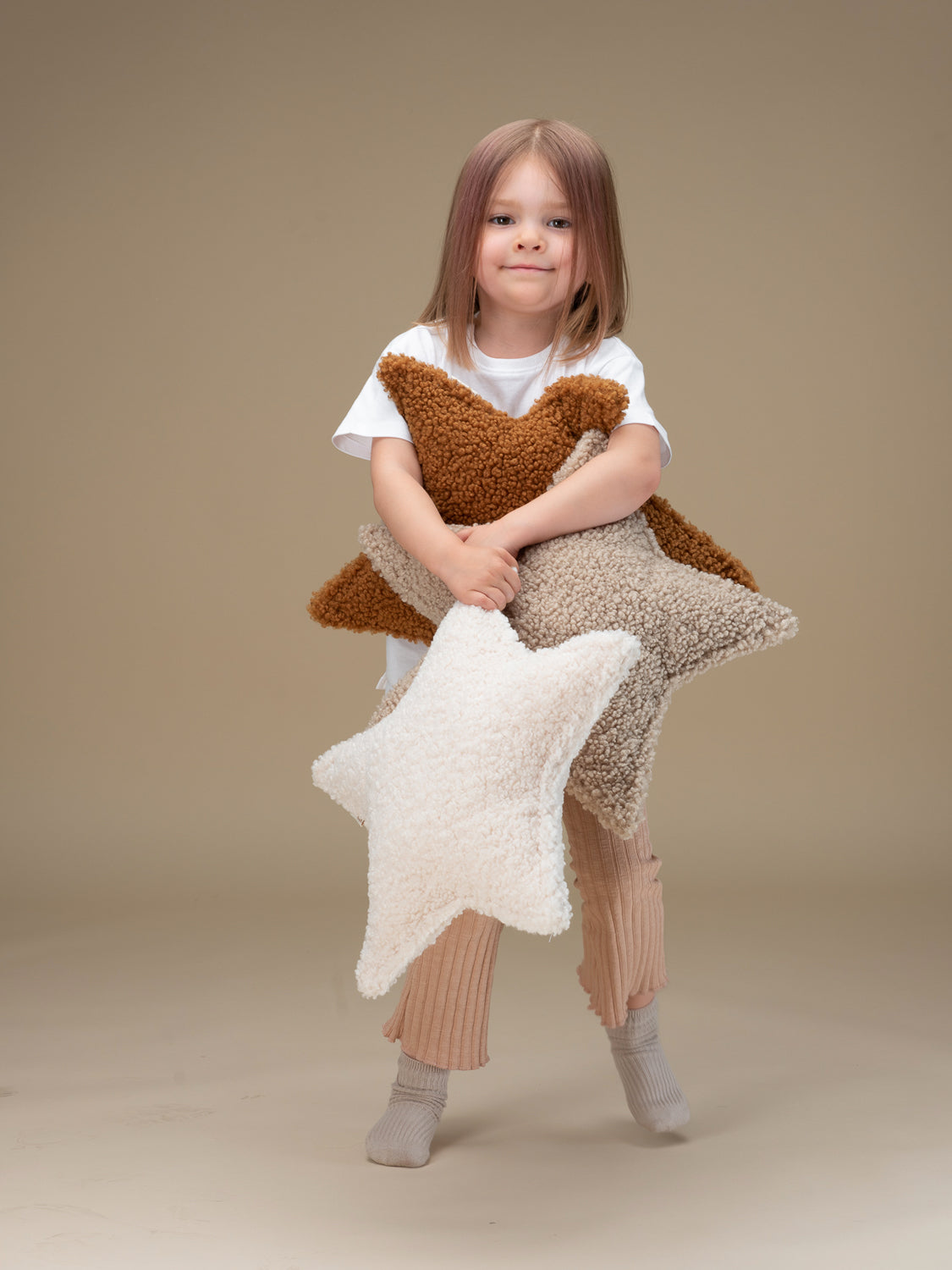 Petite fille debout tenant dans ses bras des coussins en forme d'étoile pour chambre d'enfant. Wigiwama. Décoration responsable pour chambre d'enfant.