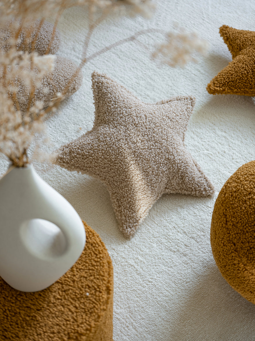 Coussin en peluche oeko-tex posé sur le sol d'une chambre d'enfant ou d'un salon dans un éclairage ensoleillé. 