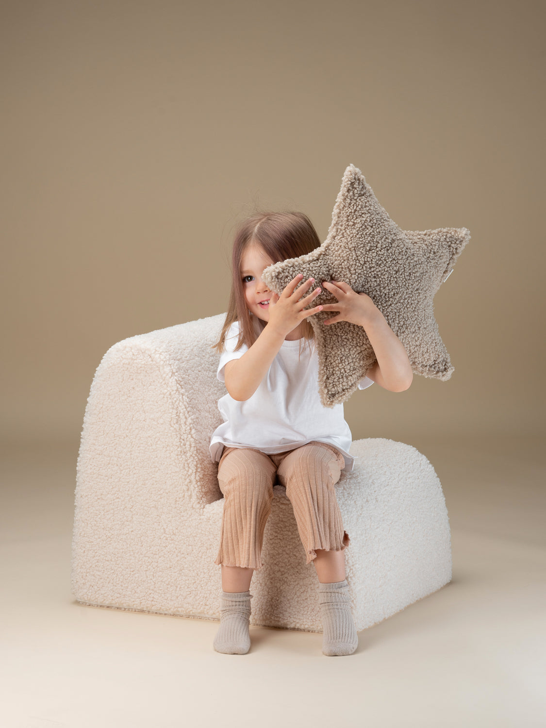 Petite fille s'amusant avec un coussin léger et doux en peluche oeko-tex de la marque Wigiwama. Coloris Biscuit, forme étoile.