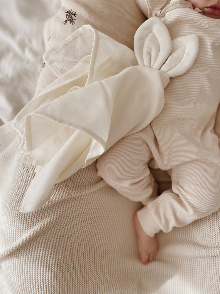 Doudou 100% coton biologique blanc cassé, écru. Ici posé à côté de bébé qui dort paisiblement. Douceur et confort. Dès la naissance.