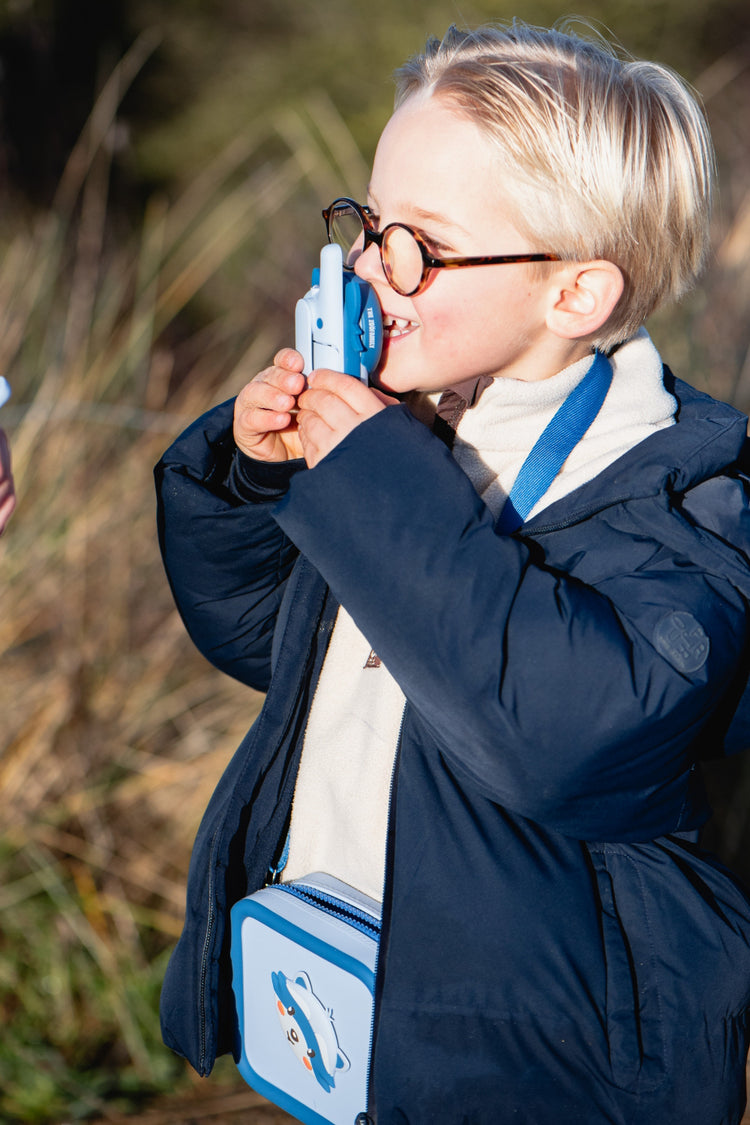 Enfant explorateur qui parle dans son talkie-walkie Raton laveur lors d'une balade dans les hautes herbes