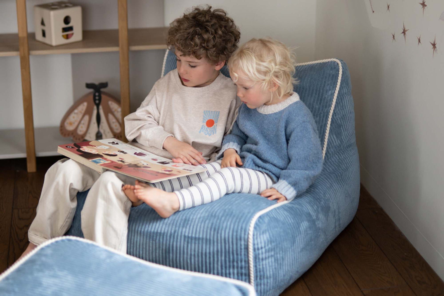 Deux enfants installés dans un fauteuil enfant bleu Shappy pour lire ensemble