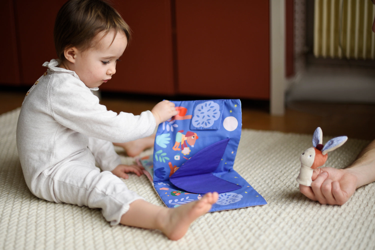 Livre en tissu pour bébé, grand format, pop up le livre s'anime à chaque page tournée avec l'apparition d'un décor. Sur la photo, un petit garçon tourne les pages de son livre, on imagine sa curiosité et on le perçoit très concentré sur l'histoire. 