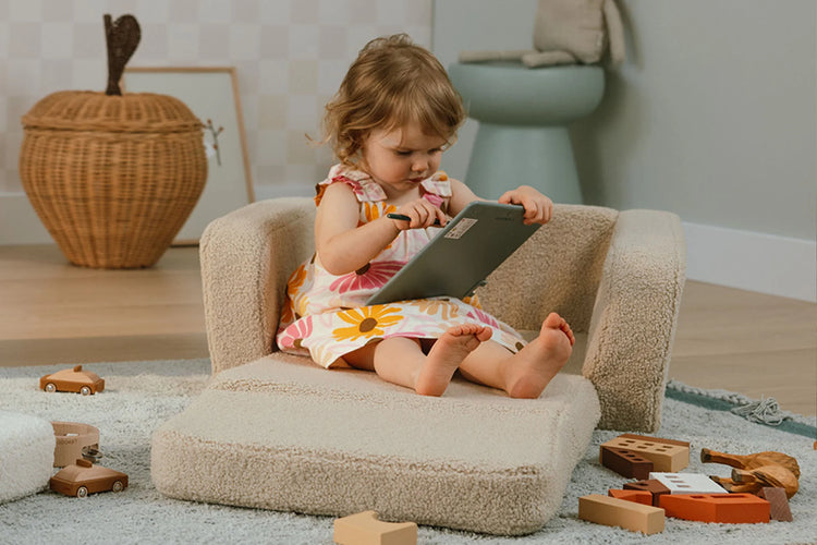 Fauteuil lecture enfant beige utilisé dans un coin lecture avec jouets.