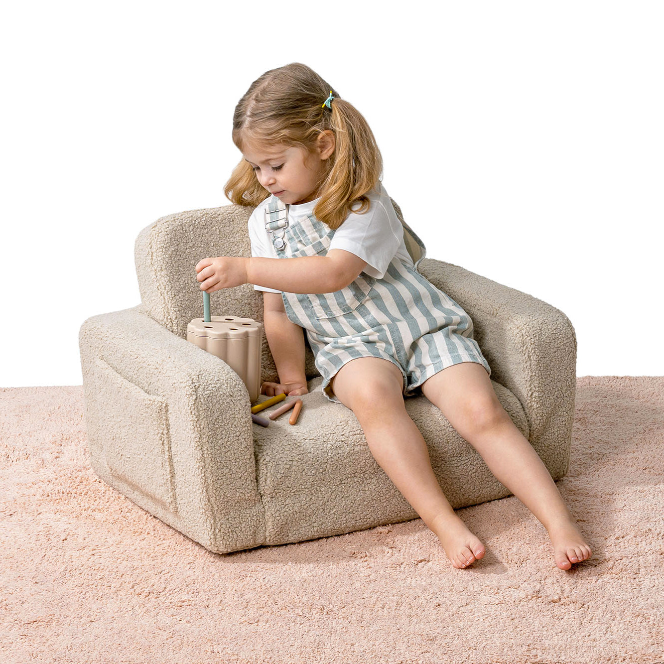 Enfant jouant assis dans un fauteuil lecture enfant beige en moumoute.
