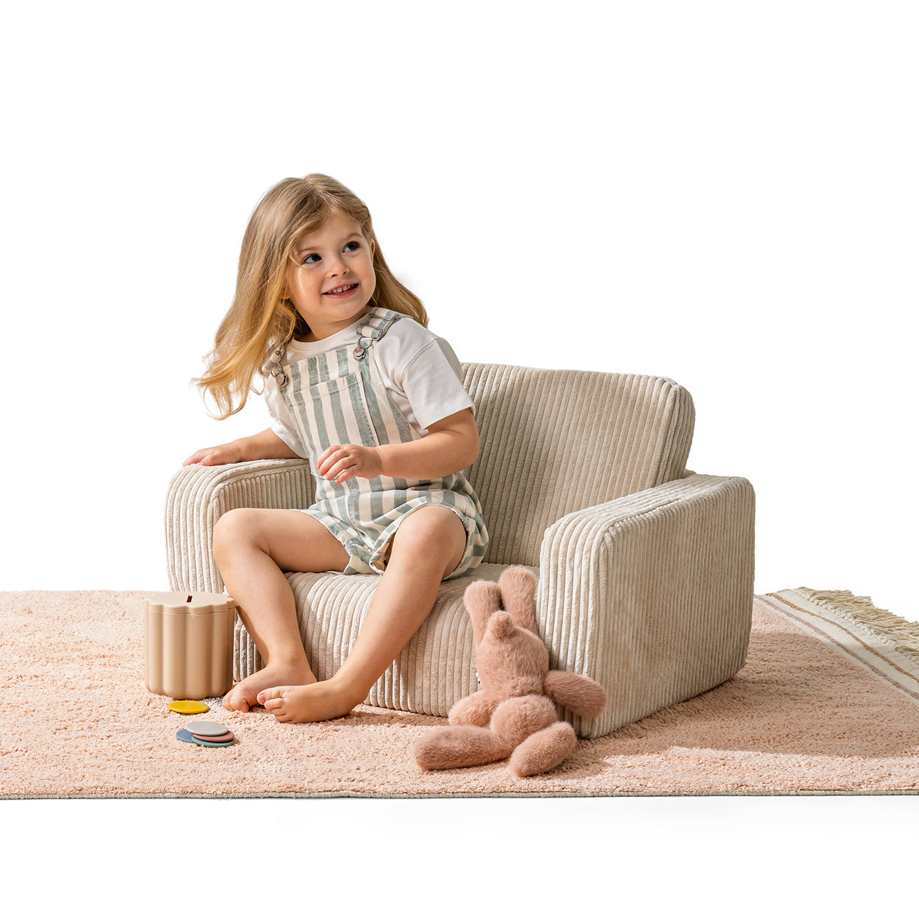 Petite fille assise confortablement dans un fauteuil enfant velours vanille avec jouets