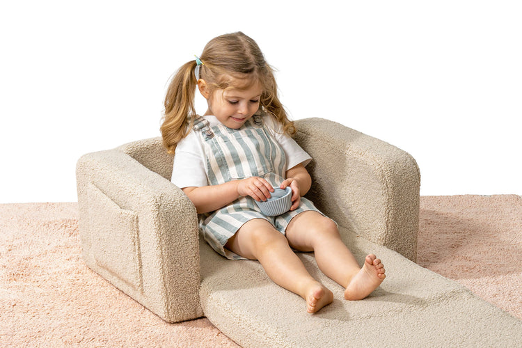Enfant confortablement installé dans un fauteuil lecture enfant beige.