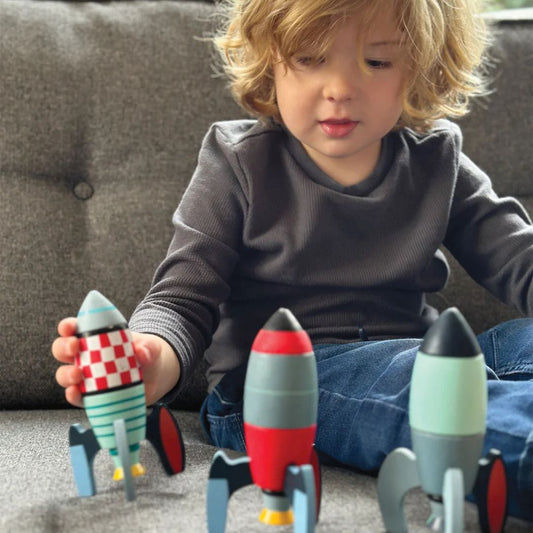 Enfant de 3 ans jouant avec trois fusées en bois à construire Tender Leaf Toys