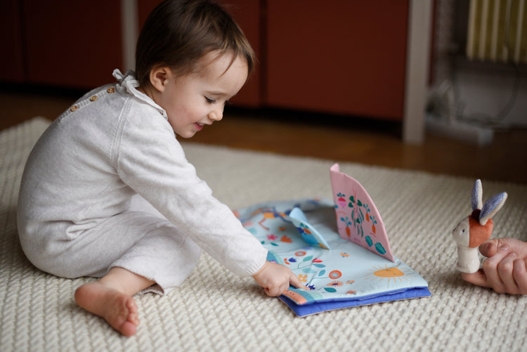 Une belle idée cadeau pour bébé : l'histoire de Gabin le lapin et sa jolie marionnette. Sur la photo : un jeune enfant, d'environ 1 an, s'amuse à identifier ce qu'il voit sur le livre : idéal pour accompagner l'apprentissage du langage, premiers mots. 