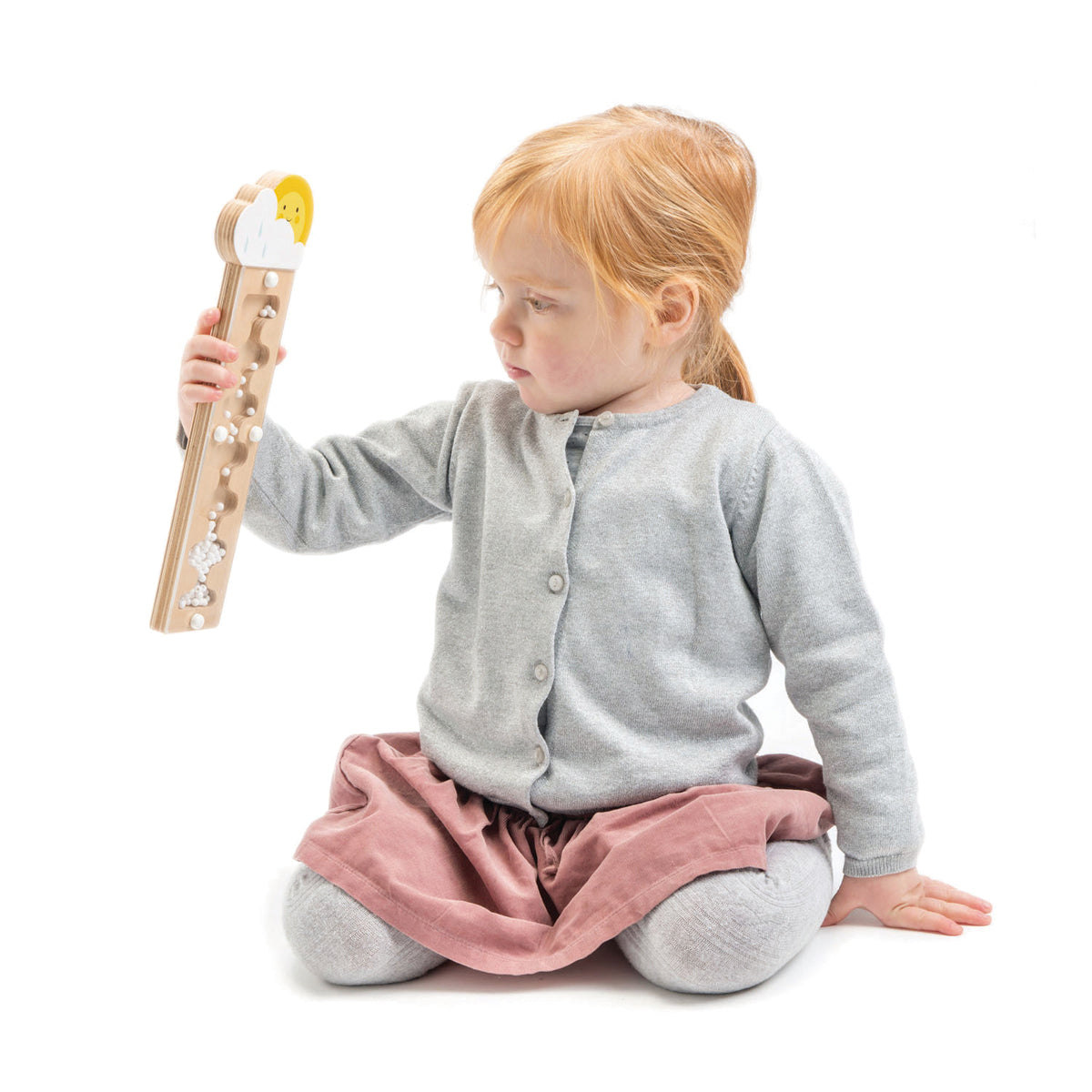 Bâton de pluie en bois pour bébé à partir de 18 mois. Petite fille manipulant le tube de pluie Tender Leaf avec attention. Idéal pour découvrir les sons et s'éveiller en s'amusant.