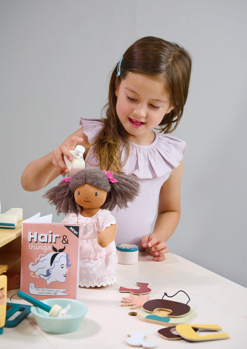 Petite fille jouant avec sa coiffeuse en bois et coiffant sa poupée