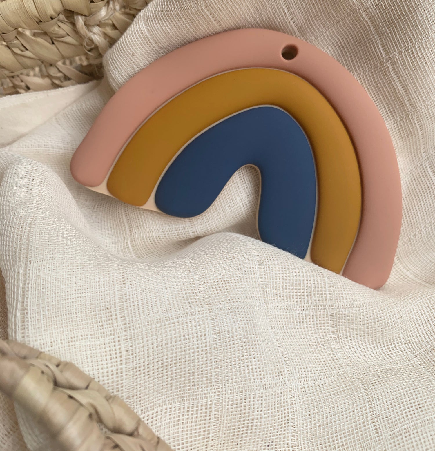 Jouet de dentition en silicone alimentaire en forme d'arc en ciel à trois couleurs douces et chaleureuses : vieux rose, jaune moutarde et bleu océan. Design minimaliste, élégant et raffiné. 