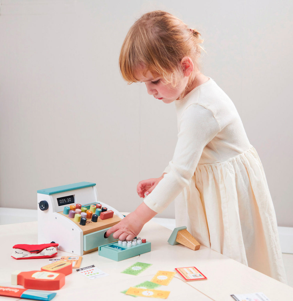 Jouet de marchande en bois naturel. Un jouet d'éveil passionnant pour les enfants dès 3 ans. Sur la photo, une petite fille se concentre et s'apprête à rendre la monnaie. 