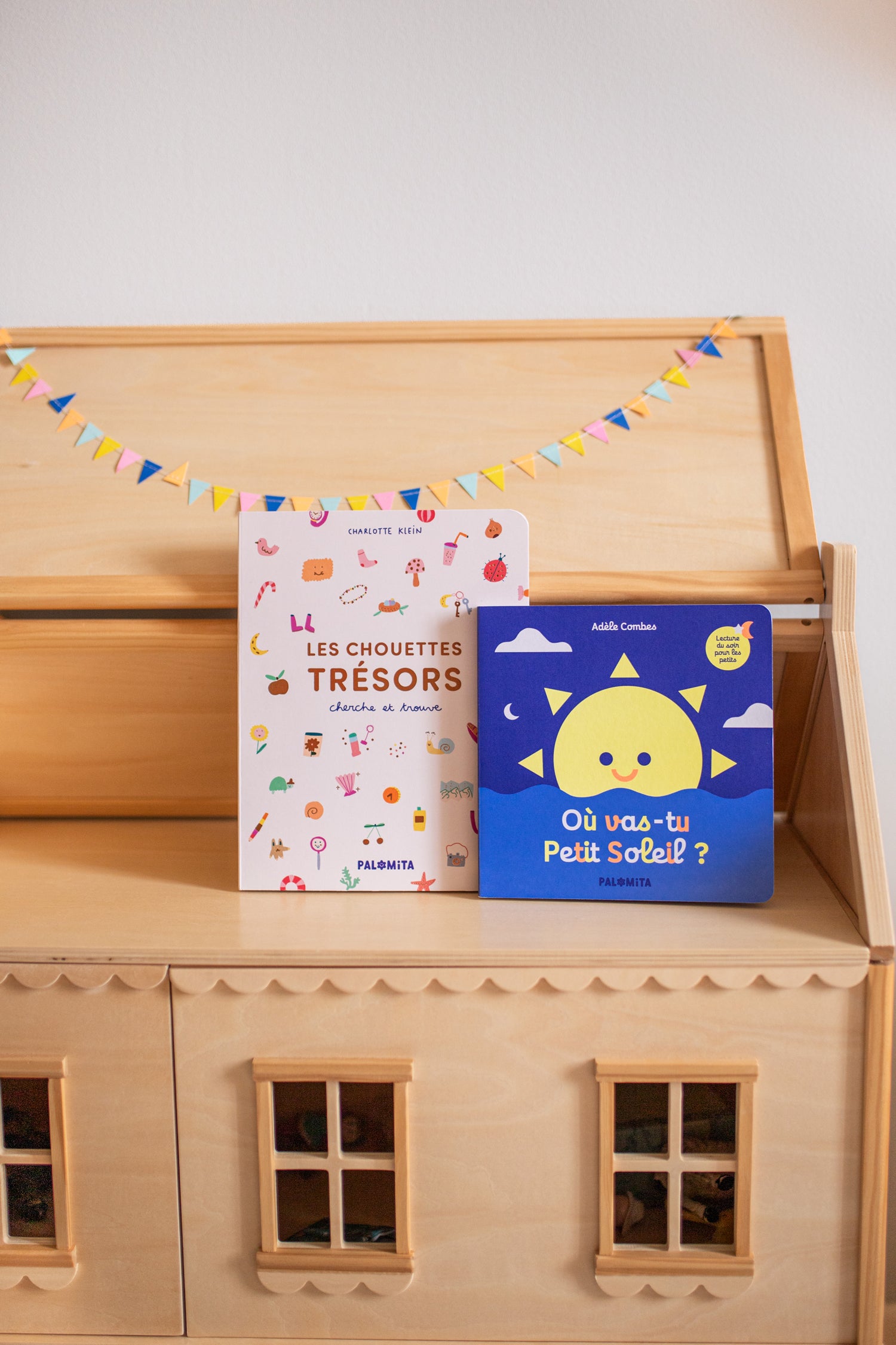 Livres pour enfants : les chouettes trésors (livre cherche et trouve) et où vas-tu petit soleil. Ici posé dans un décor de chambre d'enfants, sur une maison de poupée en bois. 