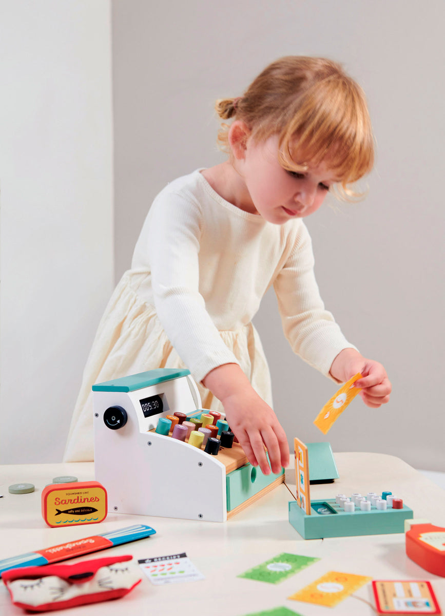 Petite fille jouant à la marchande avec la caisse enregistreuse en bois naturel d'hévéa Tender Leaf. Jeu d'imitation favoris des petits, idéal dès l'âge de 3 ans pour jouer seul ou en famille.