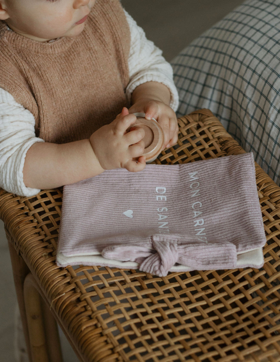 Protège carnet de santé personnalisé lila utilisé en consultation pédiatre, ordonnances rangées.