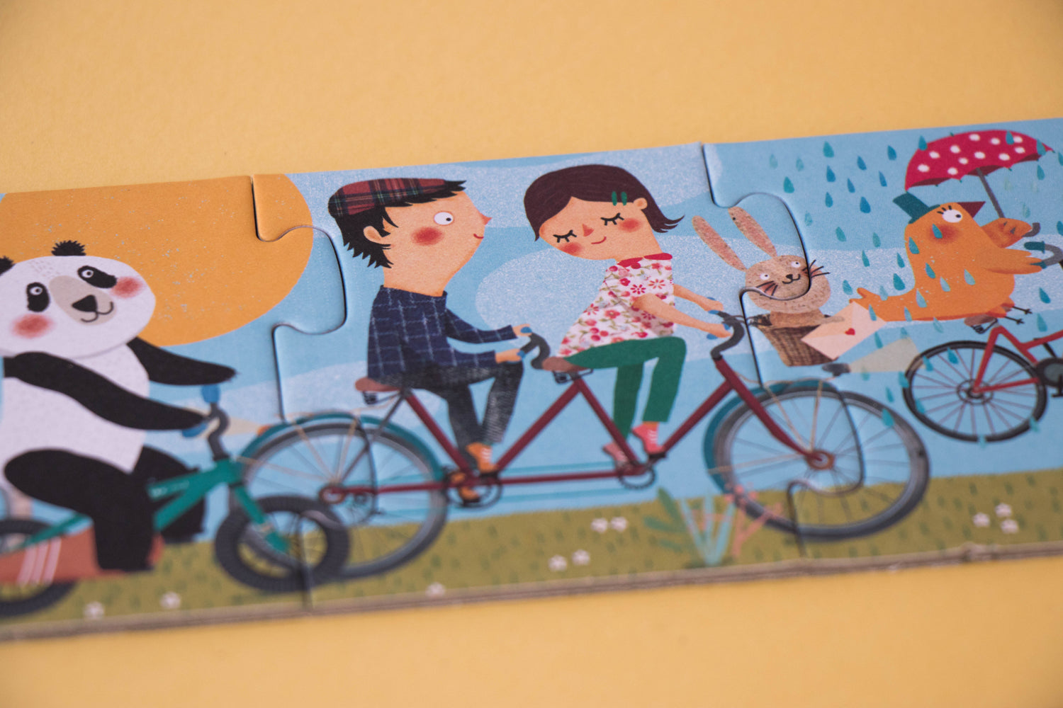 Zoom sur un morceau du puzzle évolutif Londji pour enfant dès 3 ans. Un panda sur un vélo et 2 amoureux sur un tandem. Londji Puzzles.