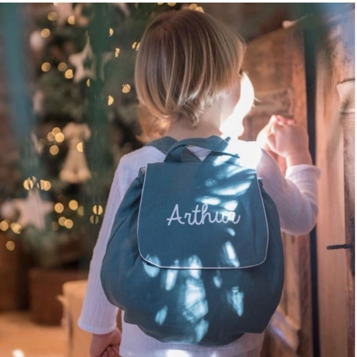 Enfant portant un sac à dos bébé crèche en lin bleu canard, prénom personnalisé : idée cadeau de naissance utile.