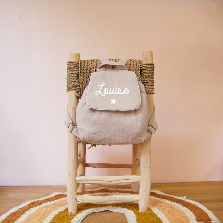 Sac à dos maternelle personnalisé beige en double gaze, motif étoile, photo ambiance sur chaise en bois.