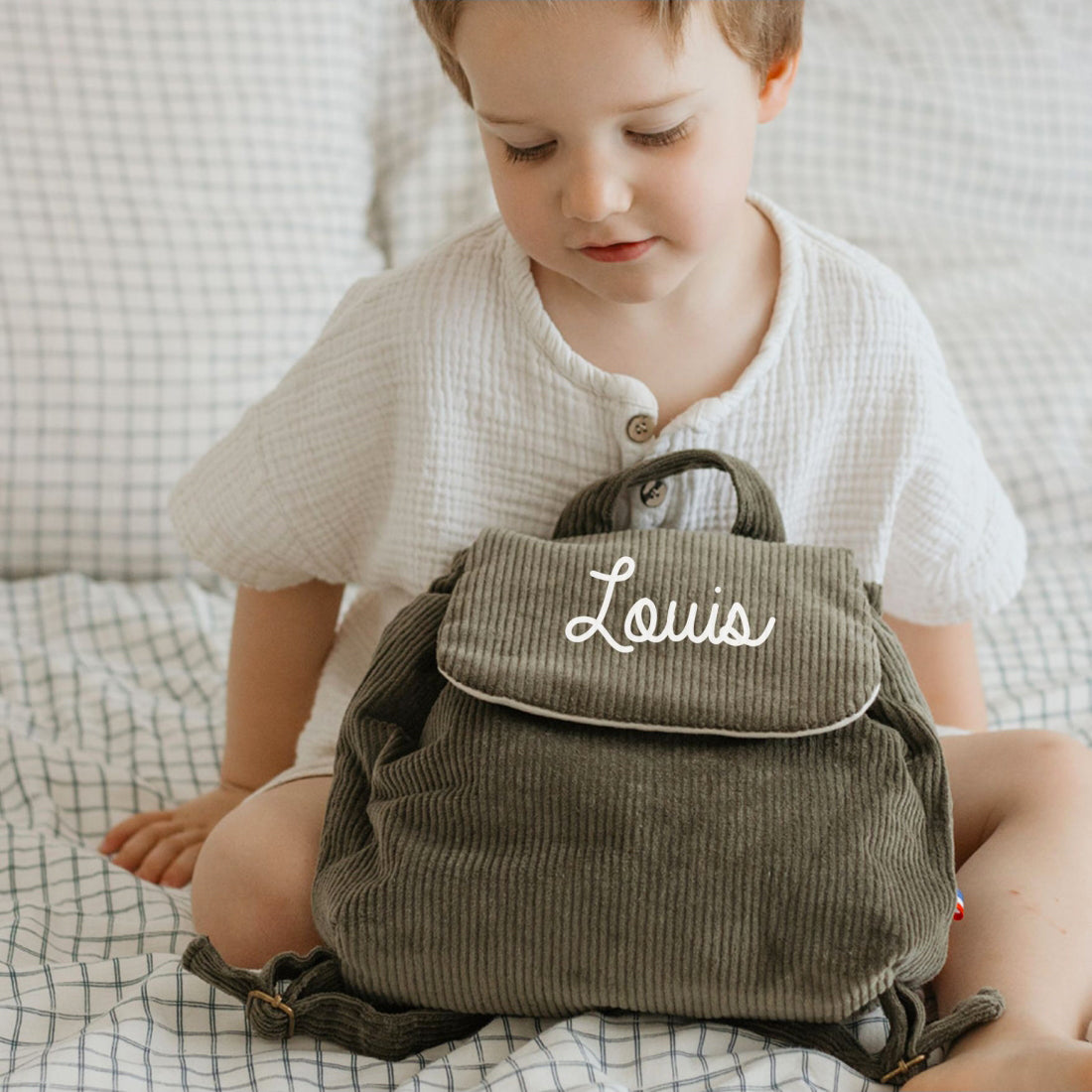 Sac à dos maternelle personnalisé velours cotele kaki posé sur les genoux d’un enfant, format compact pour doudou et goûter.