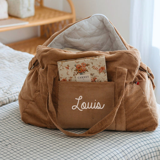 Sac de voyage bébé personnalisé en velours marron clair, prêt pour la sortie de maternité, prénom visible.
