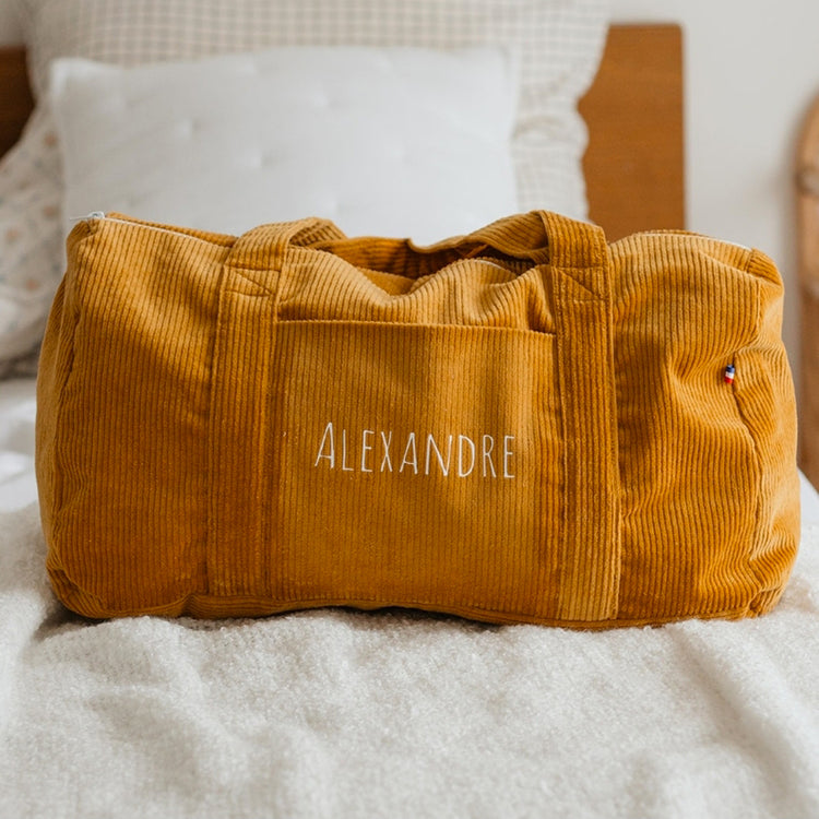 Sac week-end bébé personnalisé prêt dans la chambre, affaires rangées.
