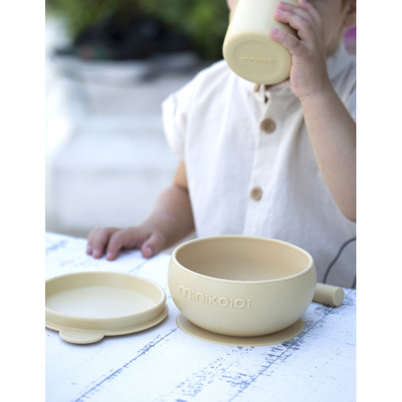 Un set de repas en silicone alimentaire durable et résistant, idéal dès le début de la découverte alimentaire. 6 mois et +. Accompagne l'enfant et le guide vers l'autonomie comme ici ou un petit garçon bois tout seul grâce au gobelet léger et facile à manipuler.