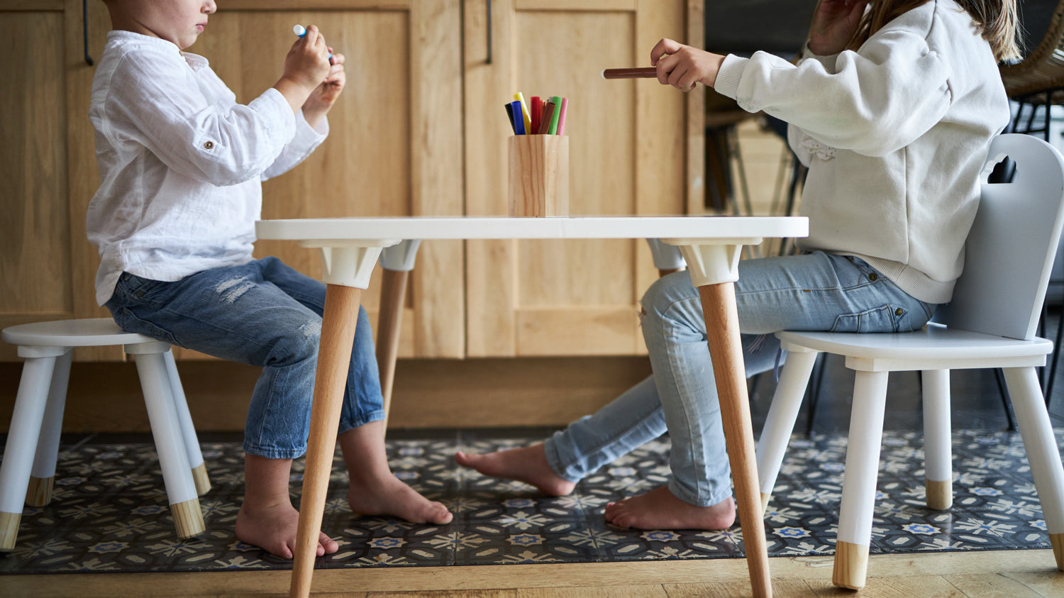 Frère et sœur installés sur une table coloriage enfant avec 2 chaises, dans un salon lumineux
