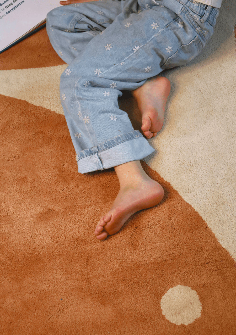 Enfant confortablement installé sur un tapis aux motifs éléphants beige et moka Bleuu-studio en coton bio.