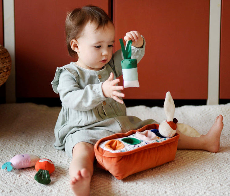 Fruits et légumes en tissu pour bébé dès l'âge de 6 mois : sur la photo une petite fille d'environ 1 an manipule avec précaution le mini-poireau au papier bruissant pour le replacer dans son emplacement.