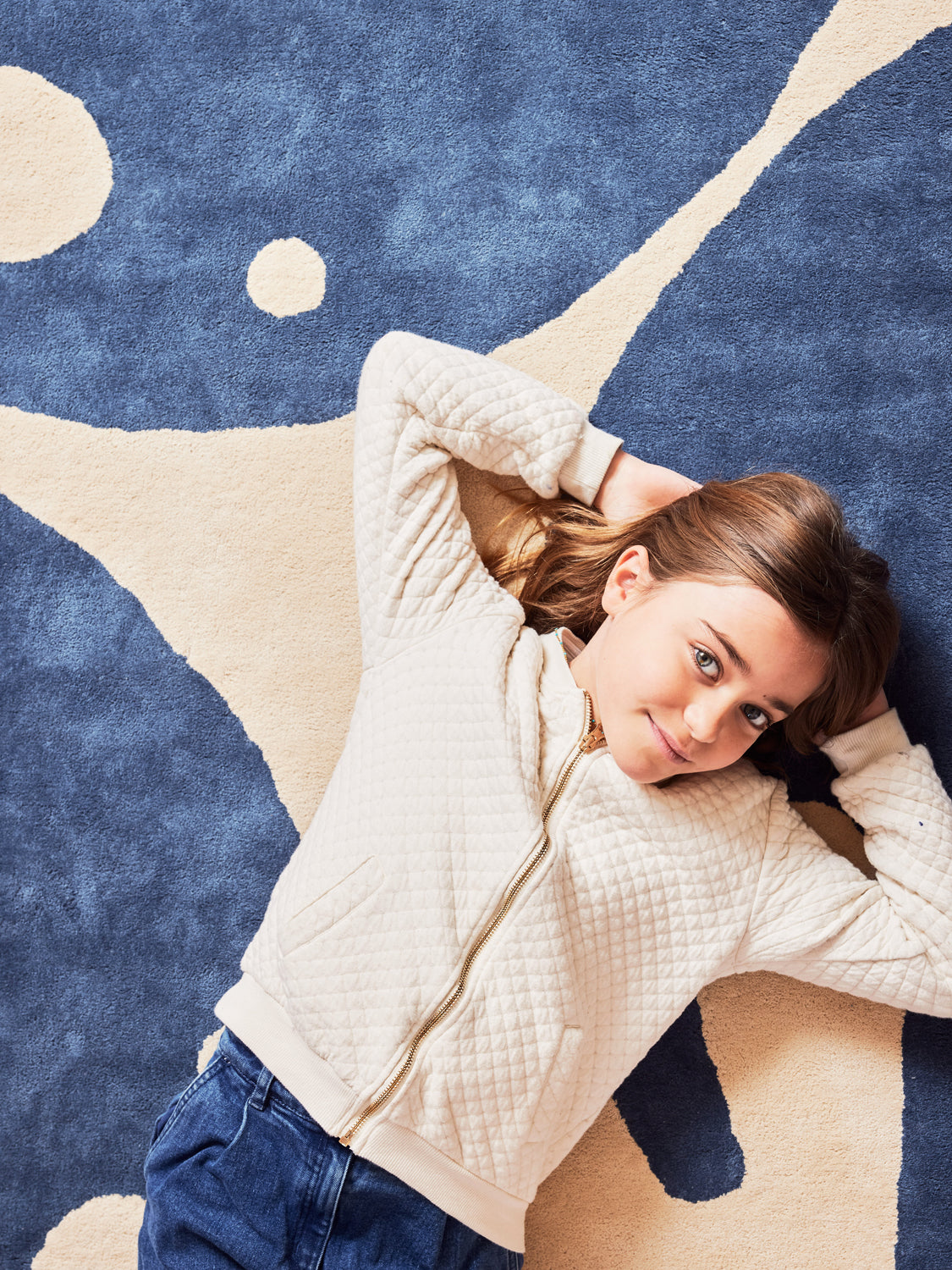 Enfant allongé sur un tapis moelleux éléphant bleu et beige. Inspiration décoration originale pour chambre enfants.