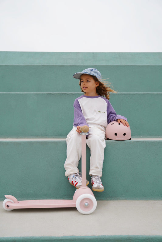 Petite fille avec trottinette rose 3 roues et casque assorti