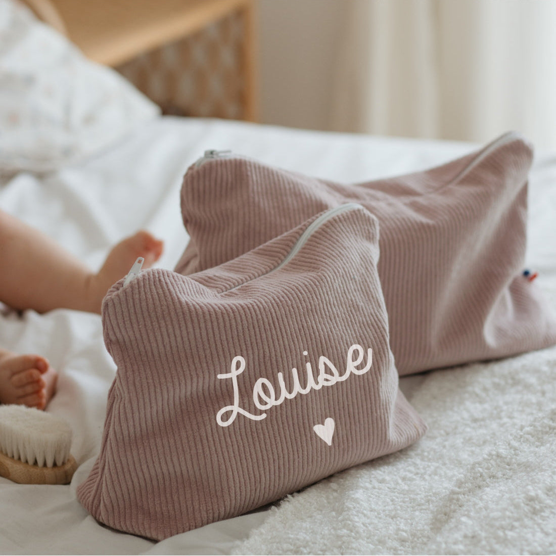 Trousse de toilette bébé personnalisée au prénom, velours côtelé lila, posée sur un lit (cadeau de naissance utile).