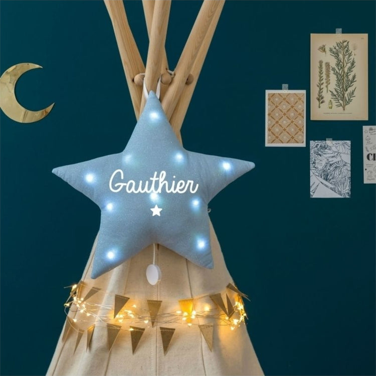Veilleuse étoile en lin bleu paillettes avec prénom Gauthier et petite étoile blanche, allumée devant un tipi.