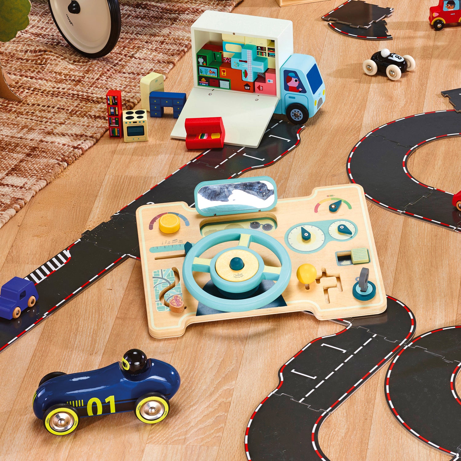 Scène de jeu dans chambre enfant, volant en bois posé au milieu des petites voitures et circuits