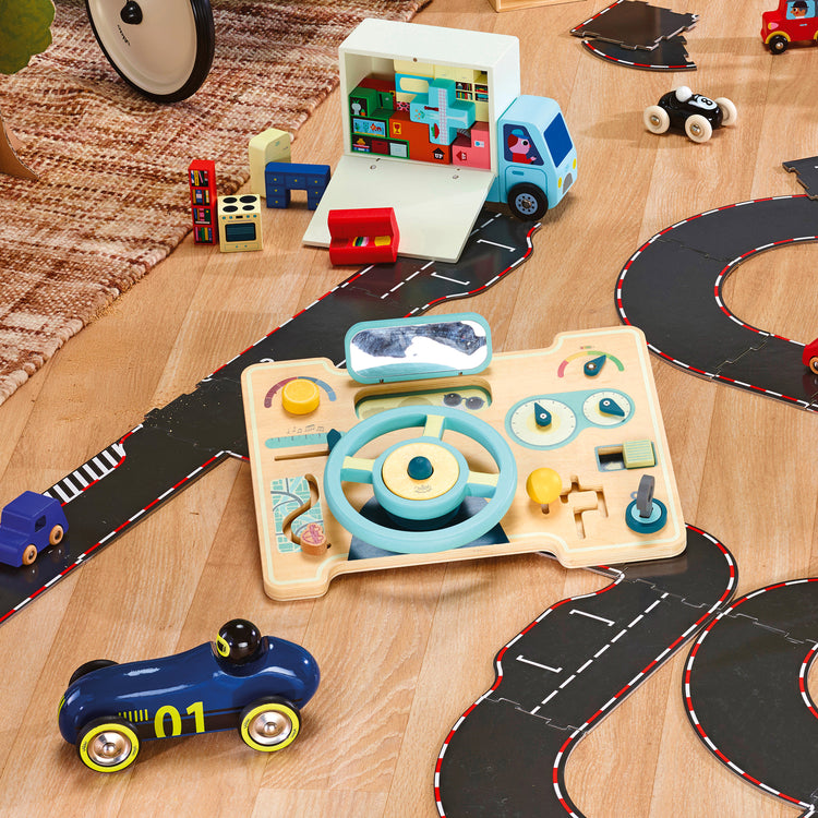 Scène de jeu dans chambre enfant, volant en bois posé au milieu des petites voitures et circuits