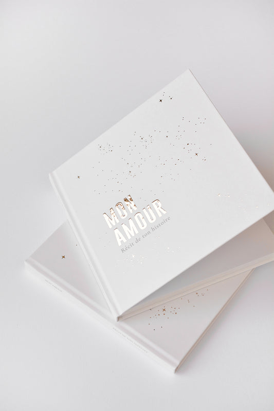 Livre de naissance Zakuw blanc et doré entre-ouvert. Design chic et épuré. Marquage doré "mon amour" brillant avec jolis reflets.