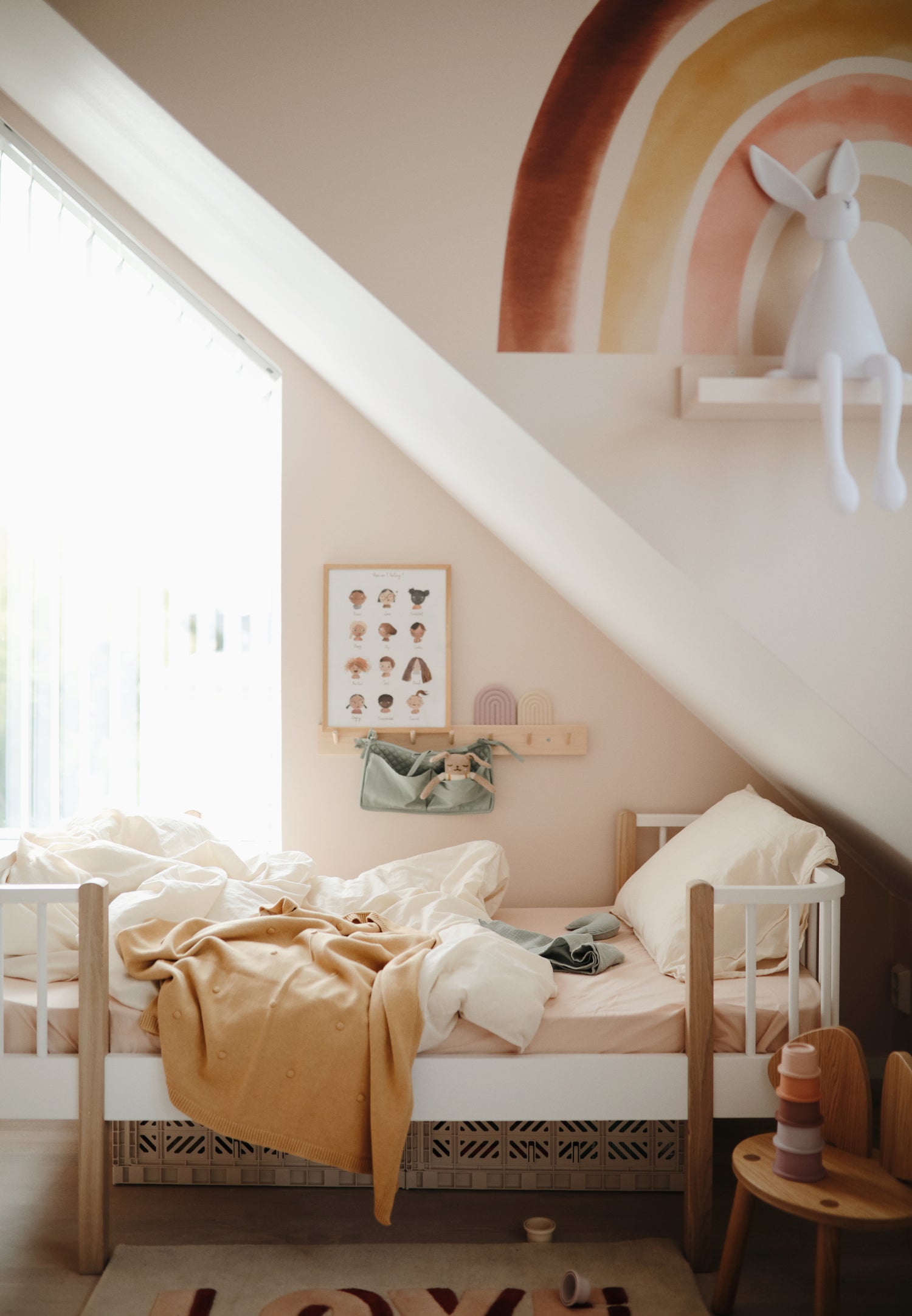 Photo ambiance : couverture mushie à pois délicatement posée sur un lit d'enfant d'environ 5 ans. Chambre aux tons pastel, rose et jaune. Meubles moderne et épuré bois et blanc. Tapis "love".